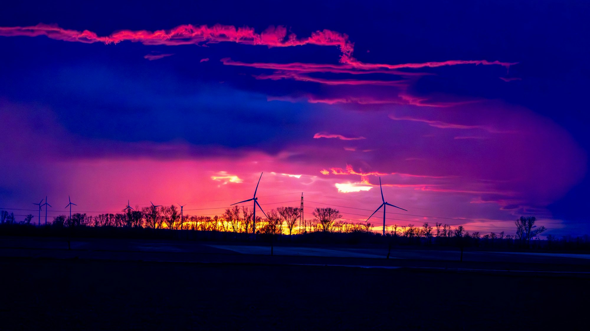 Ein Gewitter im Sonnenuntergang über dem Rhein-Erft-Kreis/Kreis Euskirchen. Im Sonnenuntergang drehen sich am Horizont Windräder.