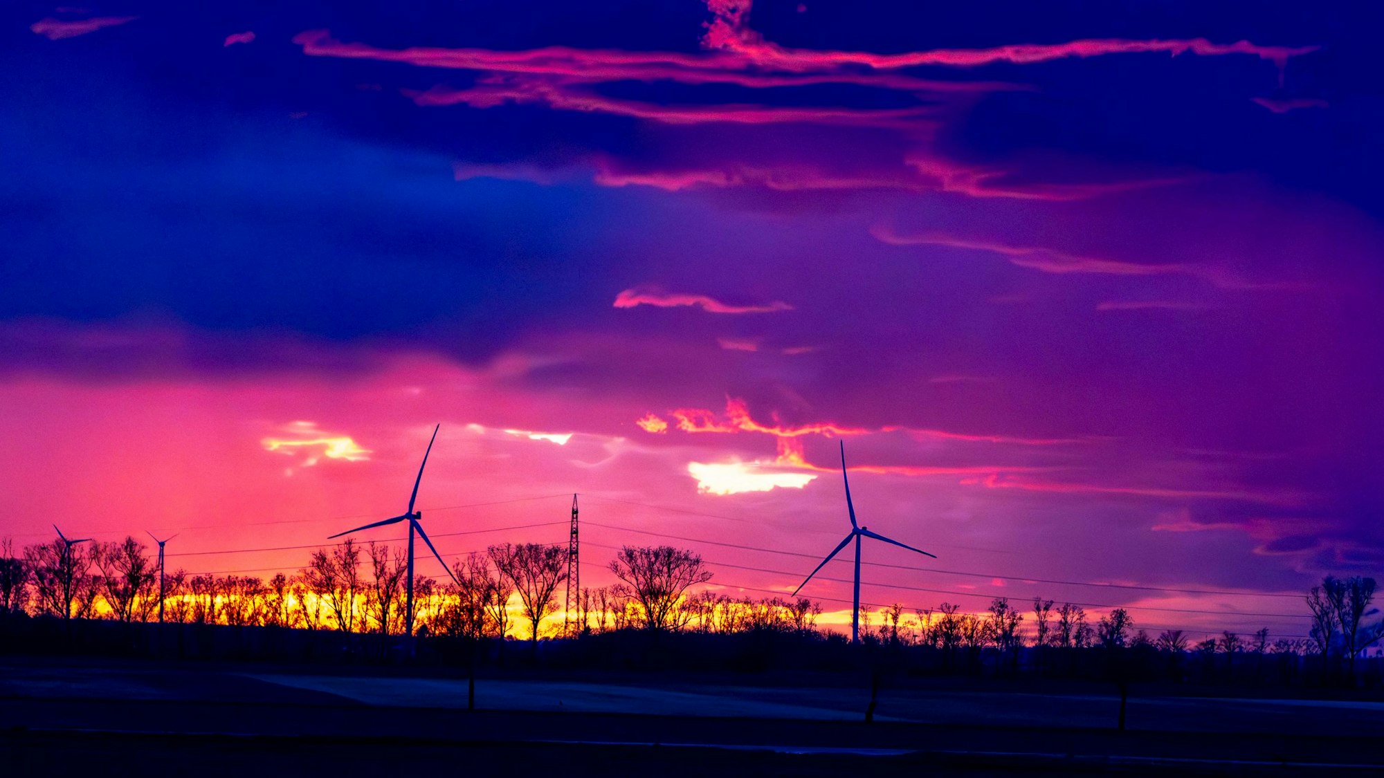 Ein Gewitter im Sonnenuntergang über dem Rhein-Erft-Kreis/Kreis Euskirchen. Im Sonnenuntergang drehen sich am Horizont Windräder.