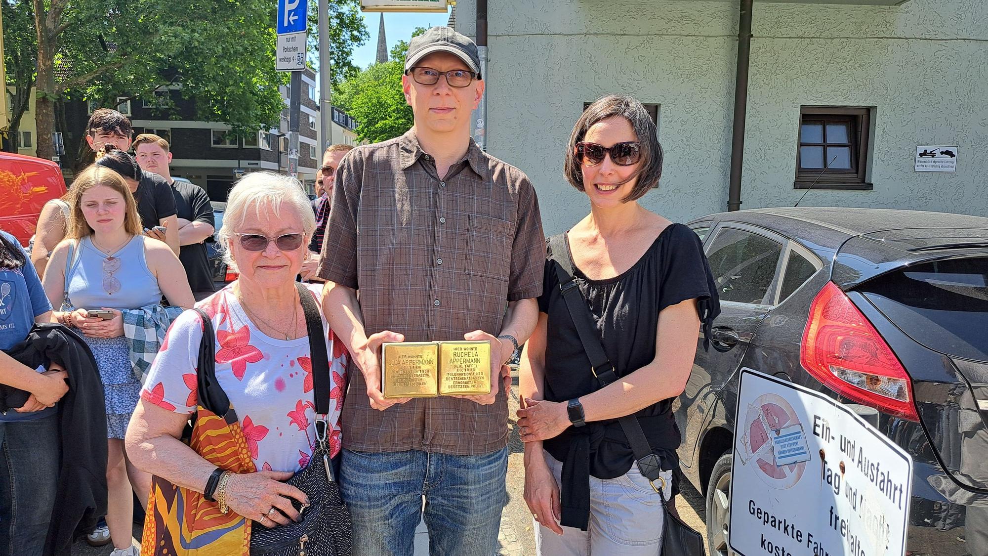 Zwei Frauen und ein Mann (Mitte) stehen nebeneinander. Der Mann hält zwei Stolpersteine in seinen Händen.