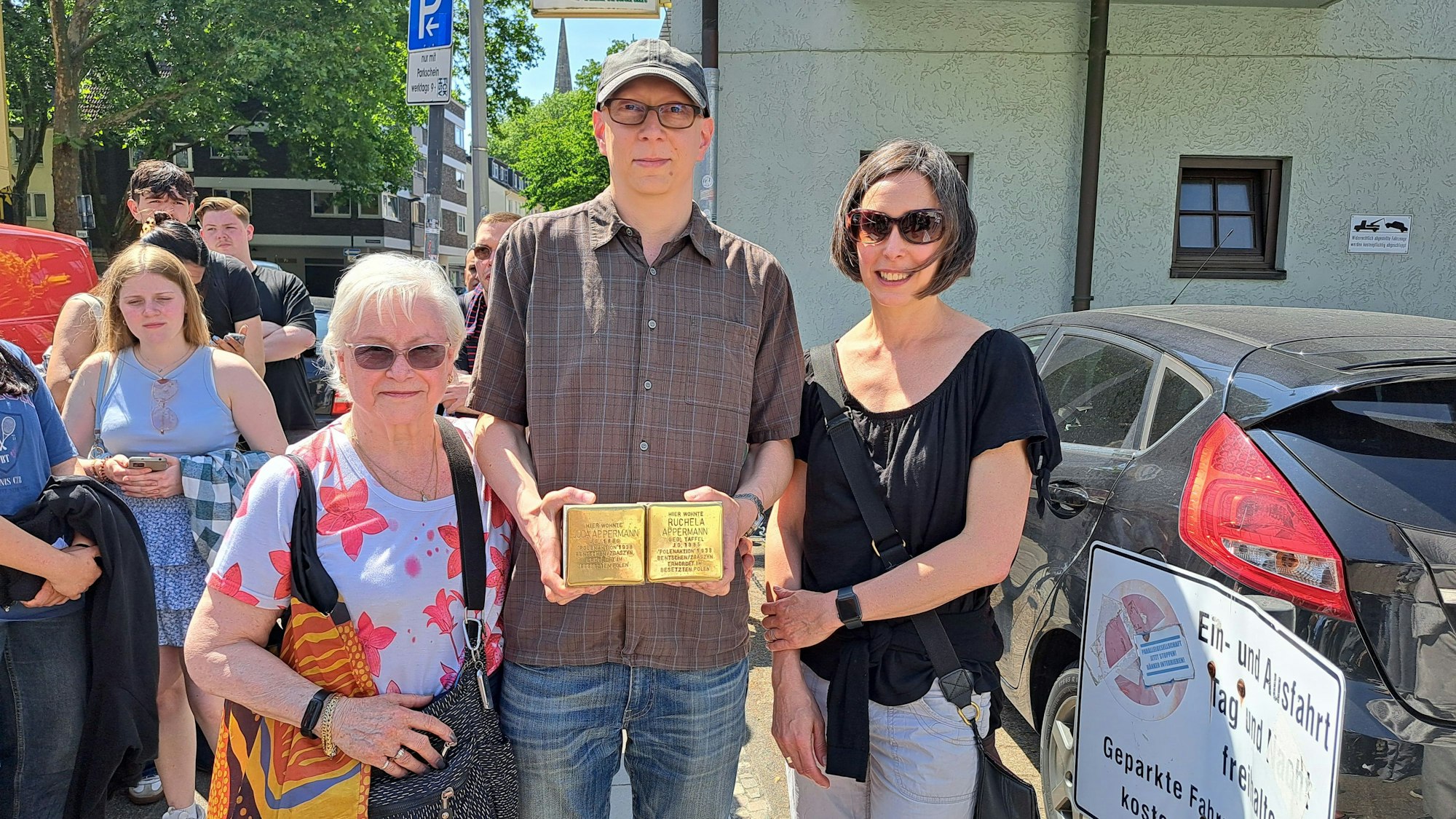 Zwei Frauen und ein Mann (Mitte) stehen nebeneinander. Der Mann hält zwei Stolpersteine in seinen Händen.