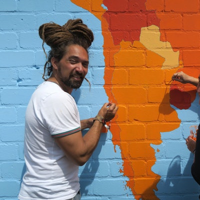 Ein Mann und eine Frau sind dabei, mit einem Pinsel den Kontinent Südamerika auszumalen, der riesig auf einer Mauer prangt.