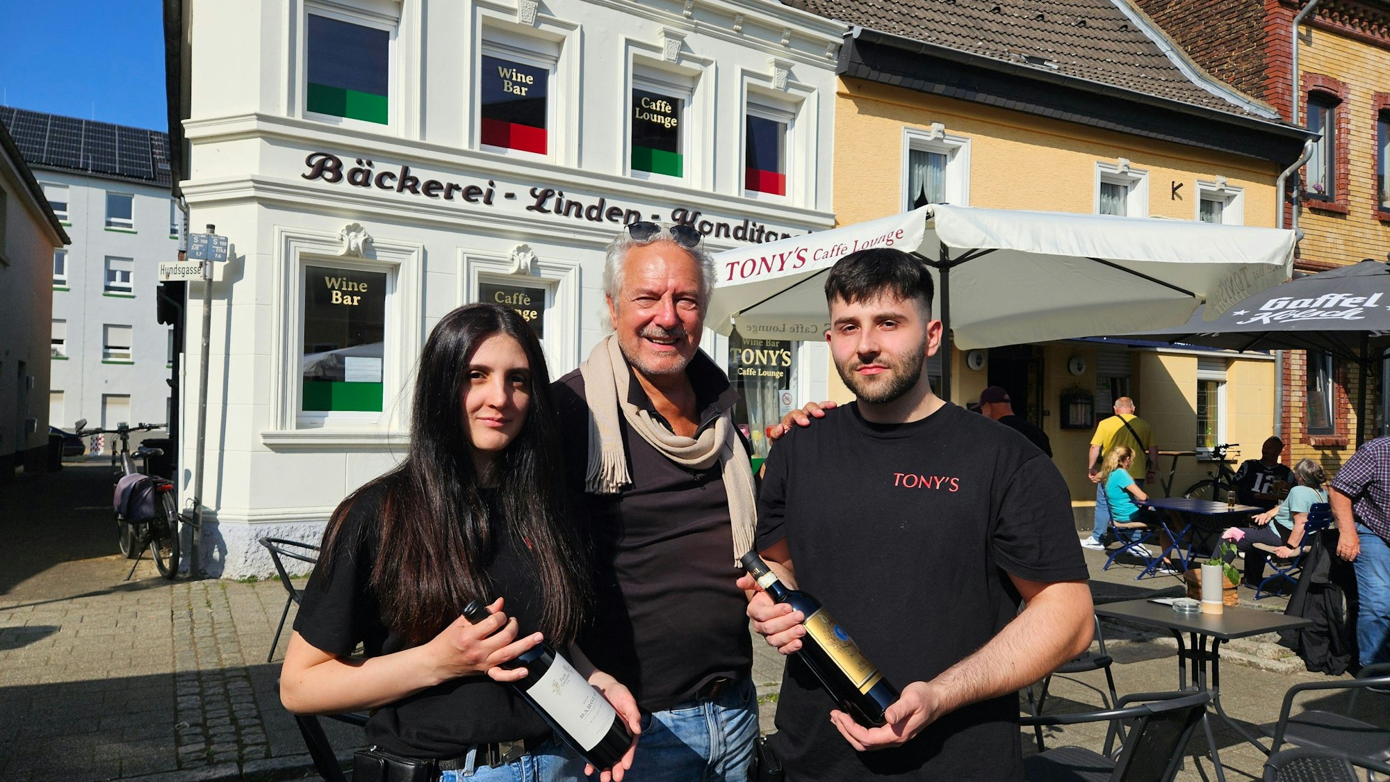 Zu sehen sind Margherita (l.) und Francesco Attrice (r.) mit jeweils einer Weinflasche in der Hand sowie in der Mitte ihr Vermieter Rolf Dieffendahl.