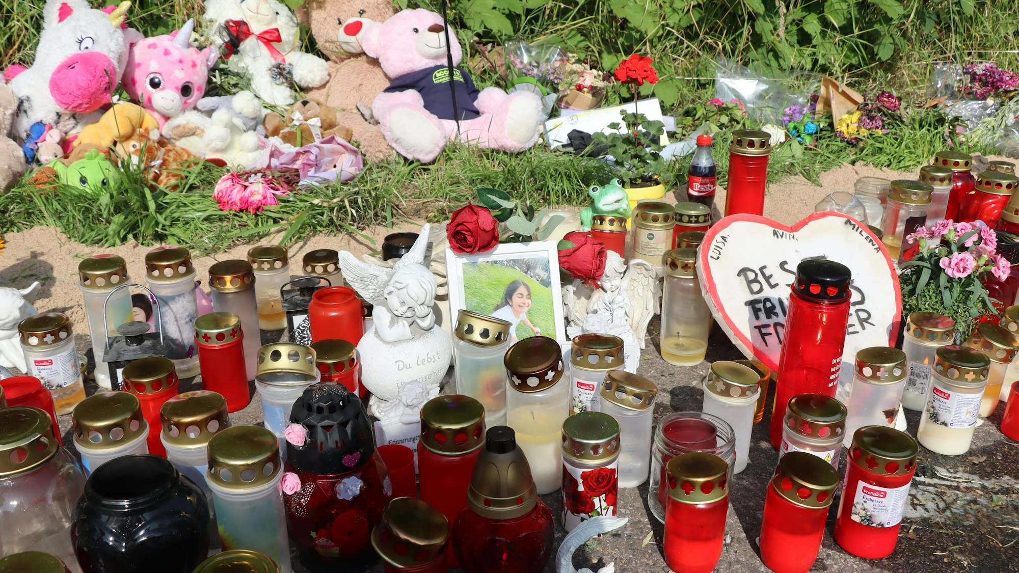Auf dem Bild ist eine Gedenkstätte mit vielen Kerzen, Stofftieren und Erinnerungsfotos zu sehen.