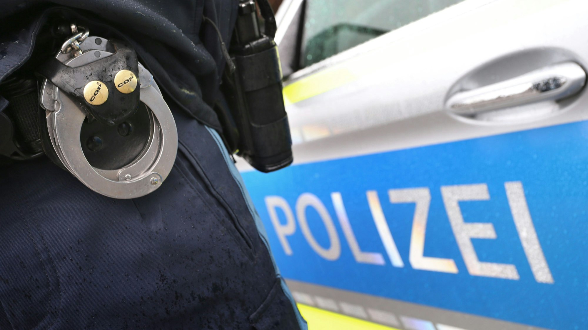 ARCHIV - 15.03.2019, Bayern, Kempten: ILLUSTRATION - Ein Polizist mit Handschellen und einer Pistole am Gürtel steht vor einem Streifenwagen. (zu dpa: «Einbrecher fragt Polizisten nach Weg - Festnahme») Foto: Karl-Josef Hildenbrand/dpa +++ dpa-Bildfunk +++