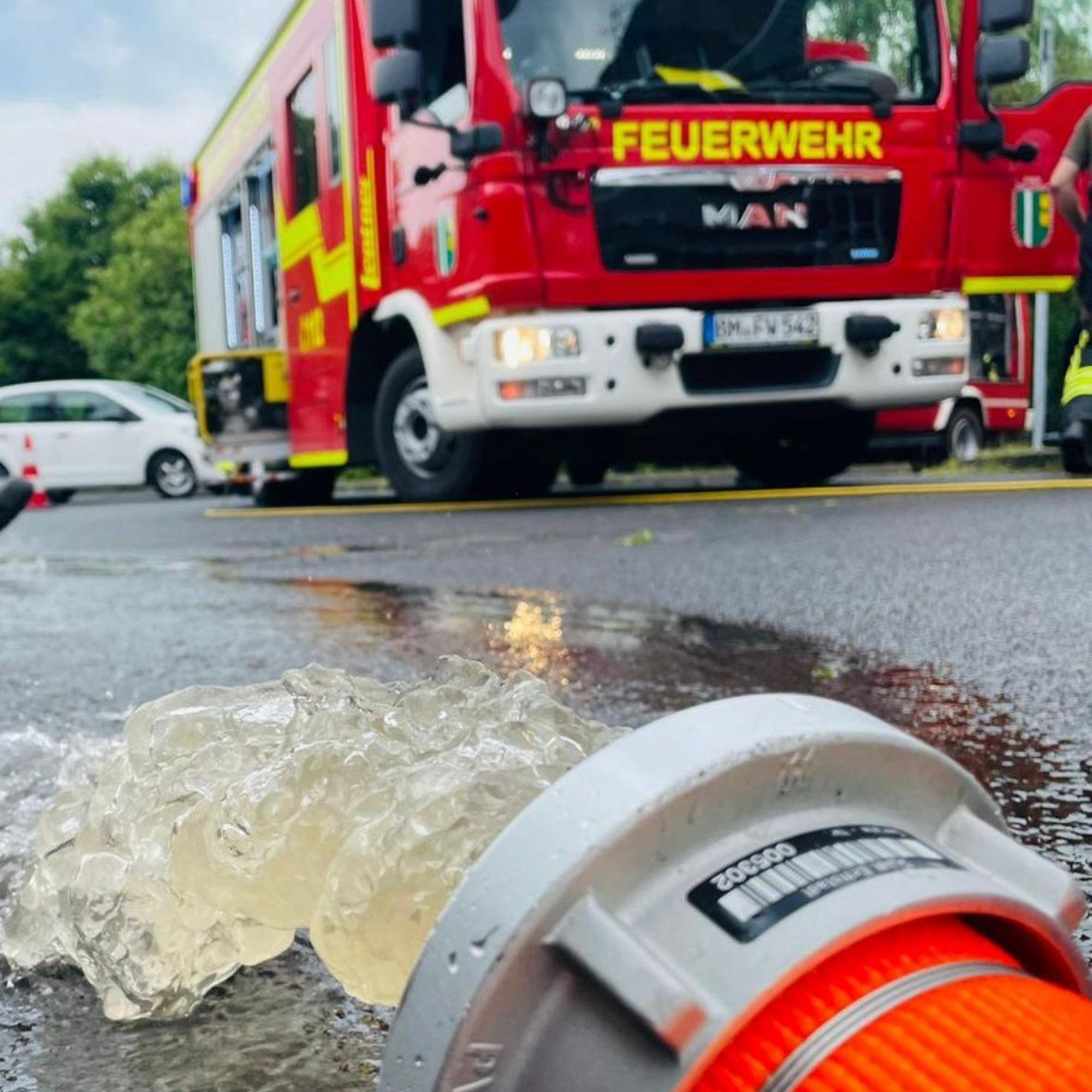 Aus einem Feuerwehrschlauch läuft Wasser auf eine Straße, im Hintergrund steht ein Einsatzwagen.