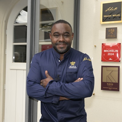 Nelson Müller steht vor der Schote, an der eine Plakette mit der Aufschrift „Michelin 2024“.