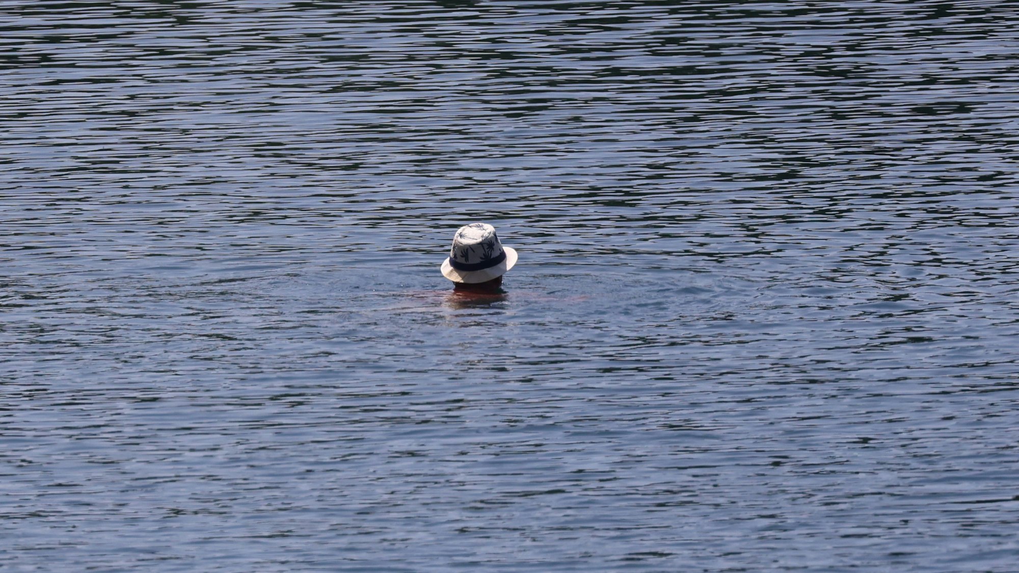 13.06.2025, Köln: Ein Schwimmer mit Hut schwimmt im Fühinger See. Köln erlebt den ersten Hitzetag des Jahres mit Temperaturen von mehr als 30°C .