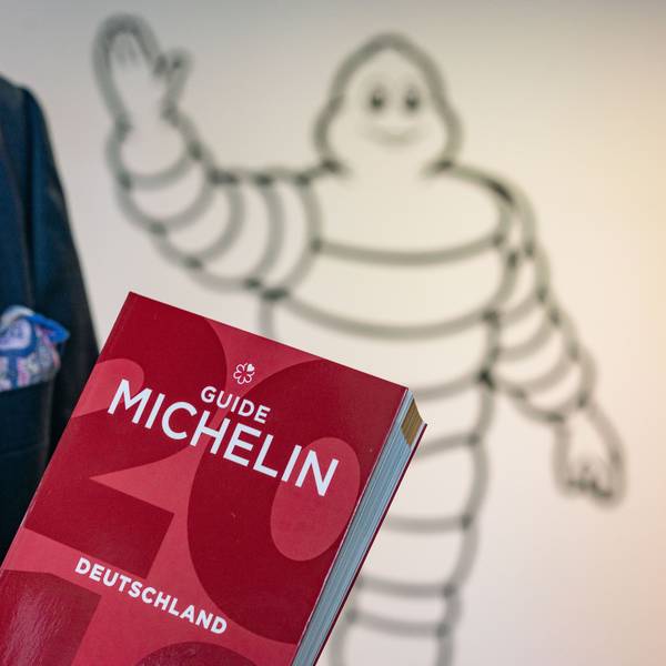 Ein roter Guide Michelin wird von einer Person im Anzug in der Hand getragen.
