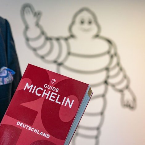 Ein roter Guide Michelin wird von einer Person im Anzug in der Hand getragen.