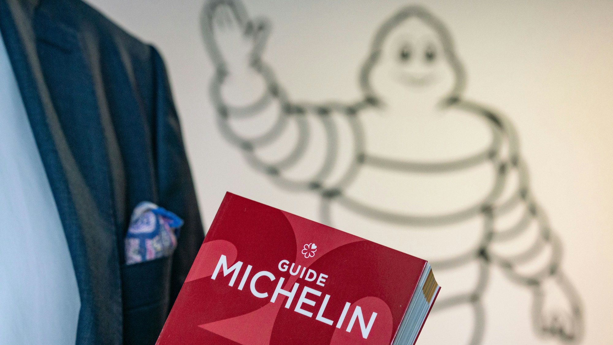 Ein roter Guide Michelin wird von einer Person im Anzug in der Hand getragen.