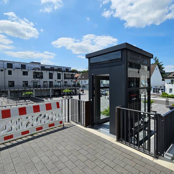 Das Bild zeigt den Aufzug und im Hintergrund den Platz und Häuser der Bahnhofstraße.