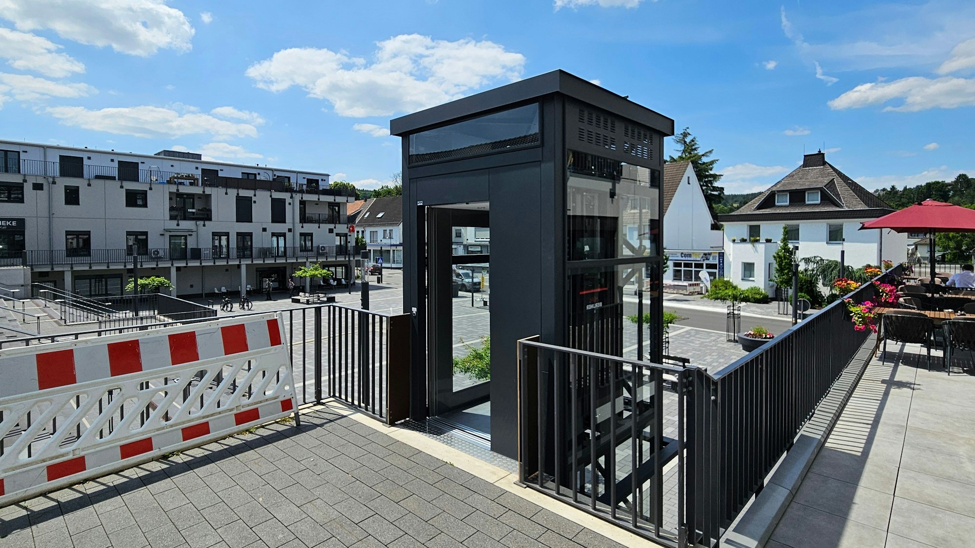 Das Bild zeigt den Aufzug und im Hintergrund den Platz und Häuser der Bahnhofstraße.