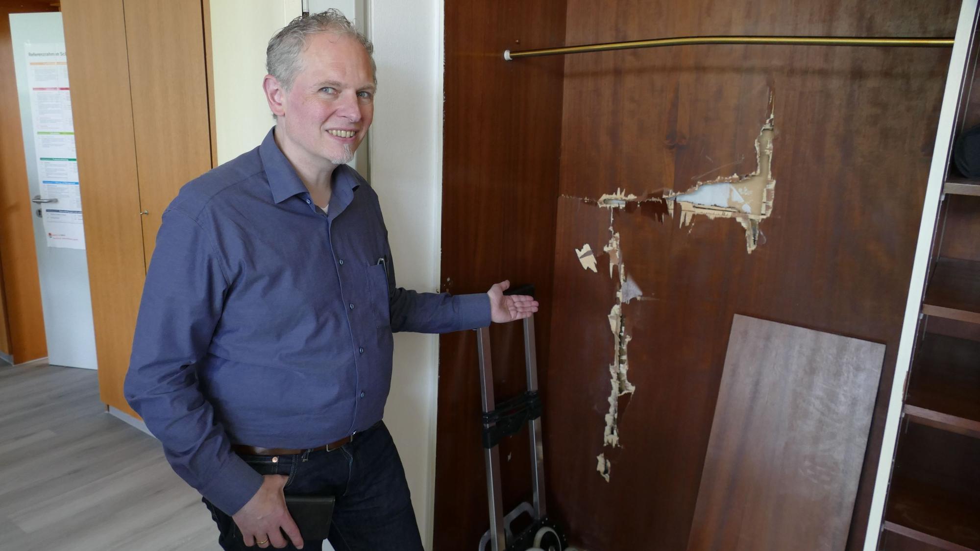 Schulleiter Sebastian Kaas zeigt die Stelle, an der Diebe einen Tresor aus der Wand gerissen haben.