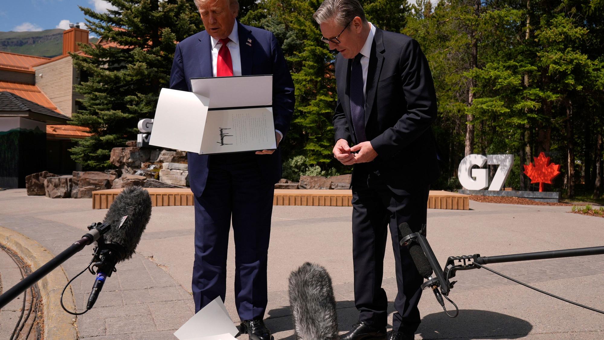 US-Präsident Donald Trump lässt Papiere fallen, als er am Rande des G7-Gipfels mit dem britischen Premierminister Keir Starmer zusammentrifft.
