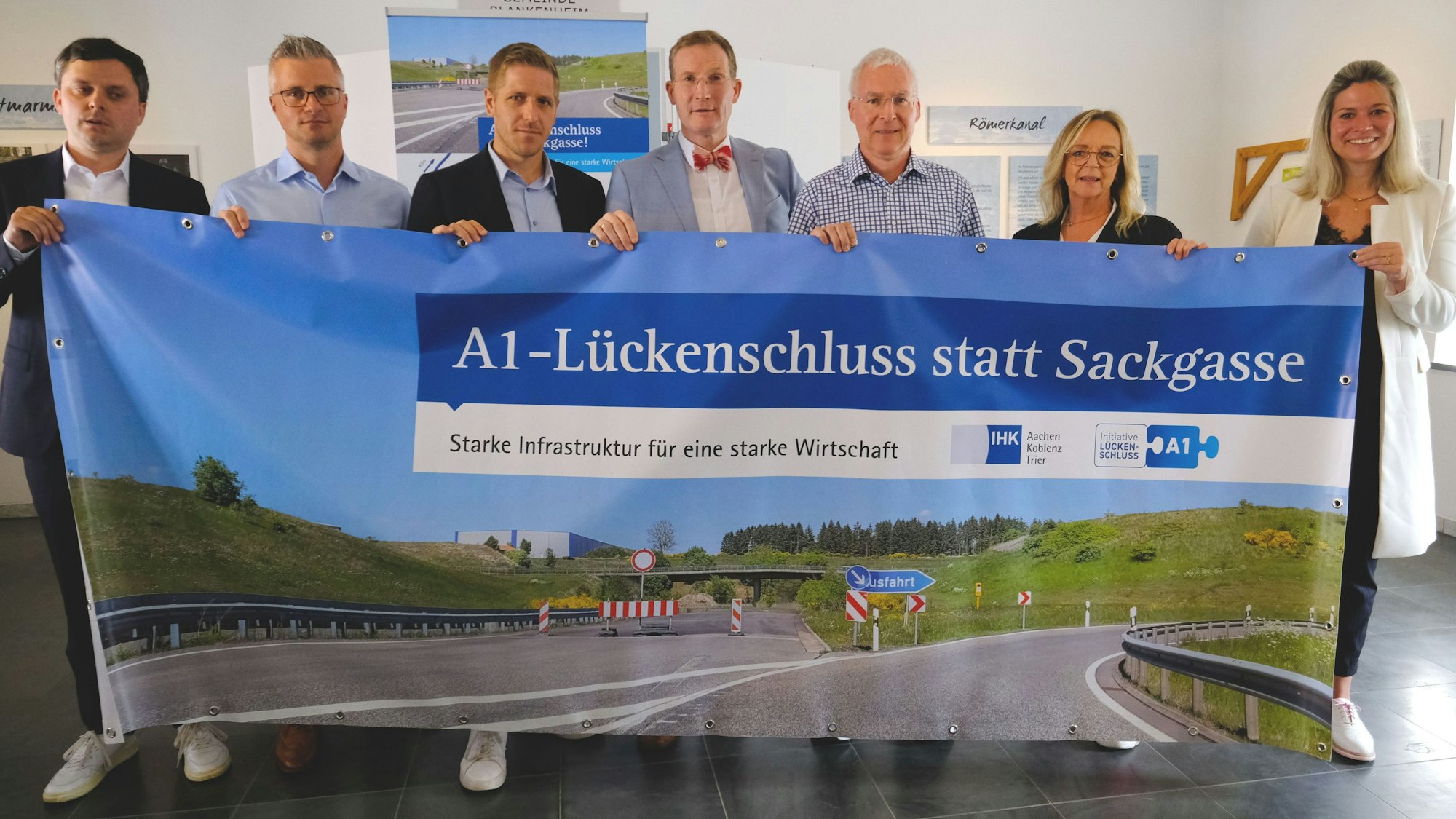 IHK-Aktion zum A1-Lückenschluss, ein entsprechendes Transparent halten v.l.n.r.):  Philipp Piecha (IHK Aachen), Daniel Claßen (Spedition Berners), Markus Ramers, Michael F. Bayer (IHK Aachen), Stephan Mahlert (Pappen Olef GmbH), Sabine Preiser-Marian (Bürgermeisterin Bad Münstereifel), Jennifer Meuren (Bürgermeisterin Blankenheim).