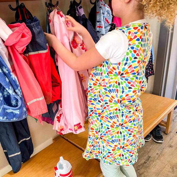 Das Symbolbild zeigt ein Kindergartenkind, das seine Jacke an der Garderobe aufhängt.