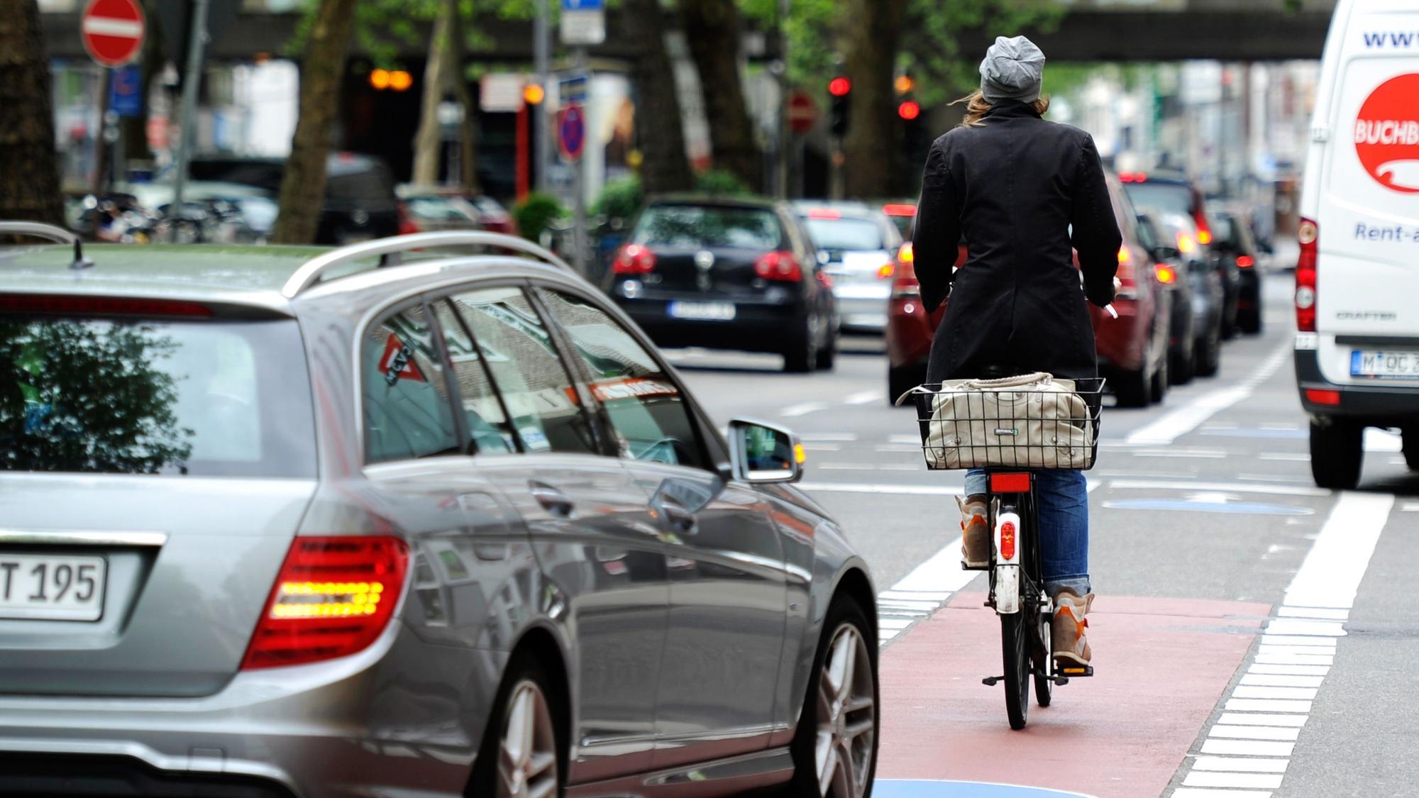 Eine Frau fährt mit ihrem Fahrrad neben Autos auf einer Straße in Köln.