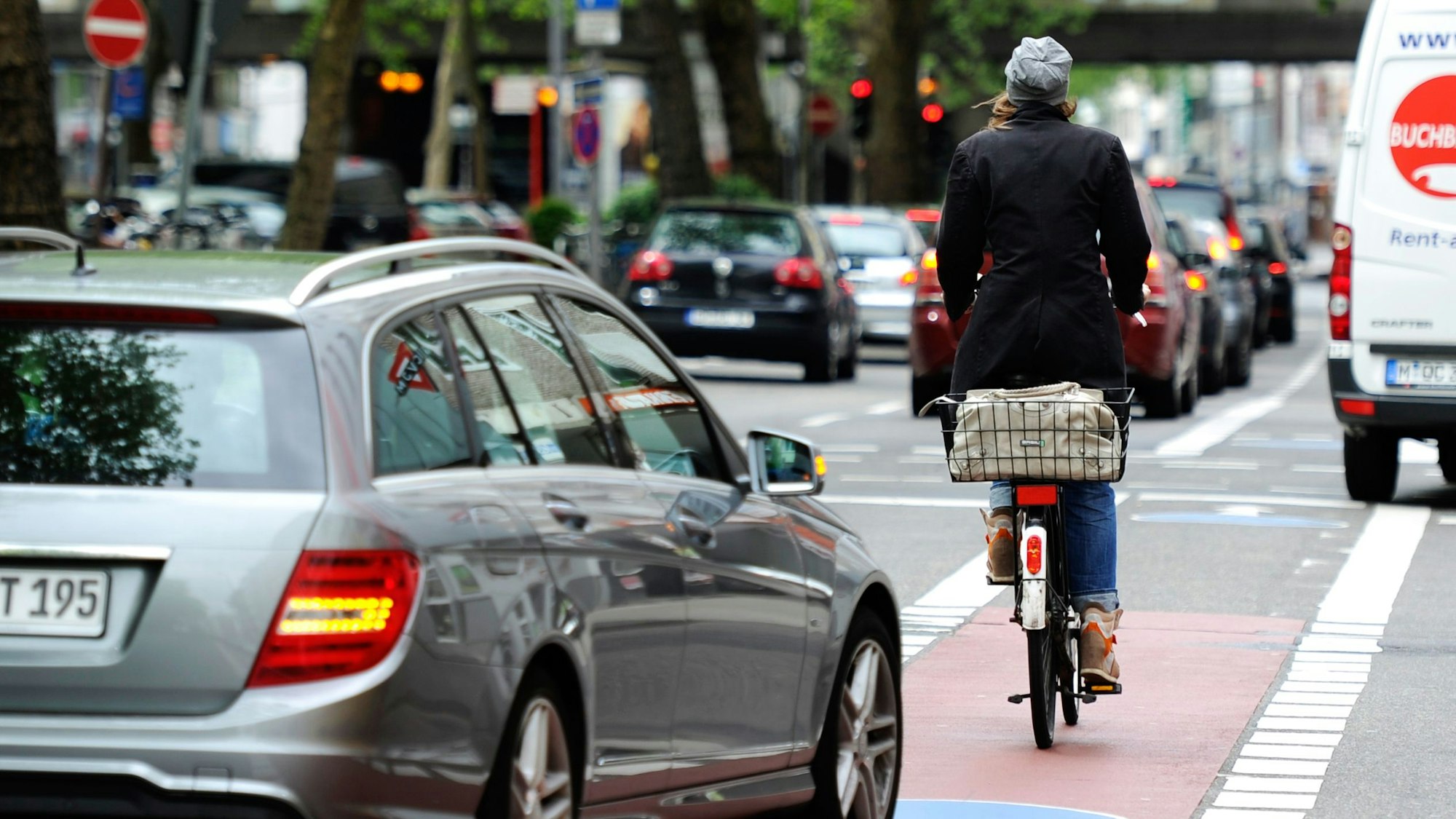 Eine Frau fährt mit ihrem Fahrrad neben Autos auf einer Straße in Köln.