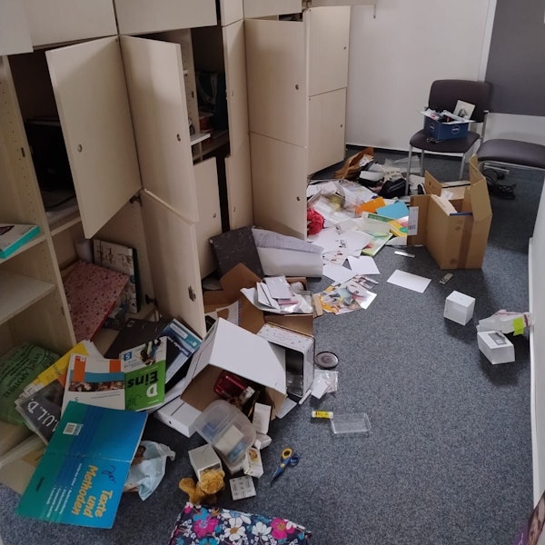 Ordner, Papier, Bücher, Kartons liegen verteilt auf dem Boden des Schulraums. Schranktüren stehen offen.
