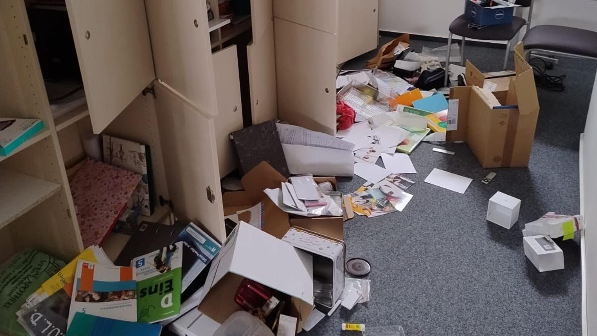Ordner, Papier, Bücher, Kartons liegen verteilt auf dem Boden des Schulraums. Schranktüren stehen offen.