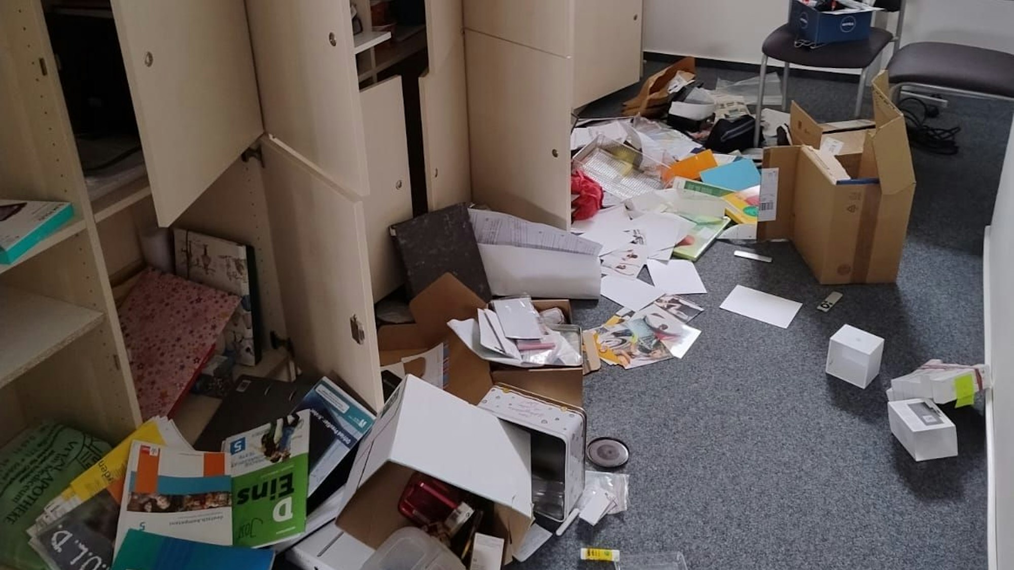 Ordner, Papier, Bücher, Kartons liegen verteilt auf dem Boden des Schulraums. Schranktüren stehen offen.