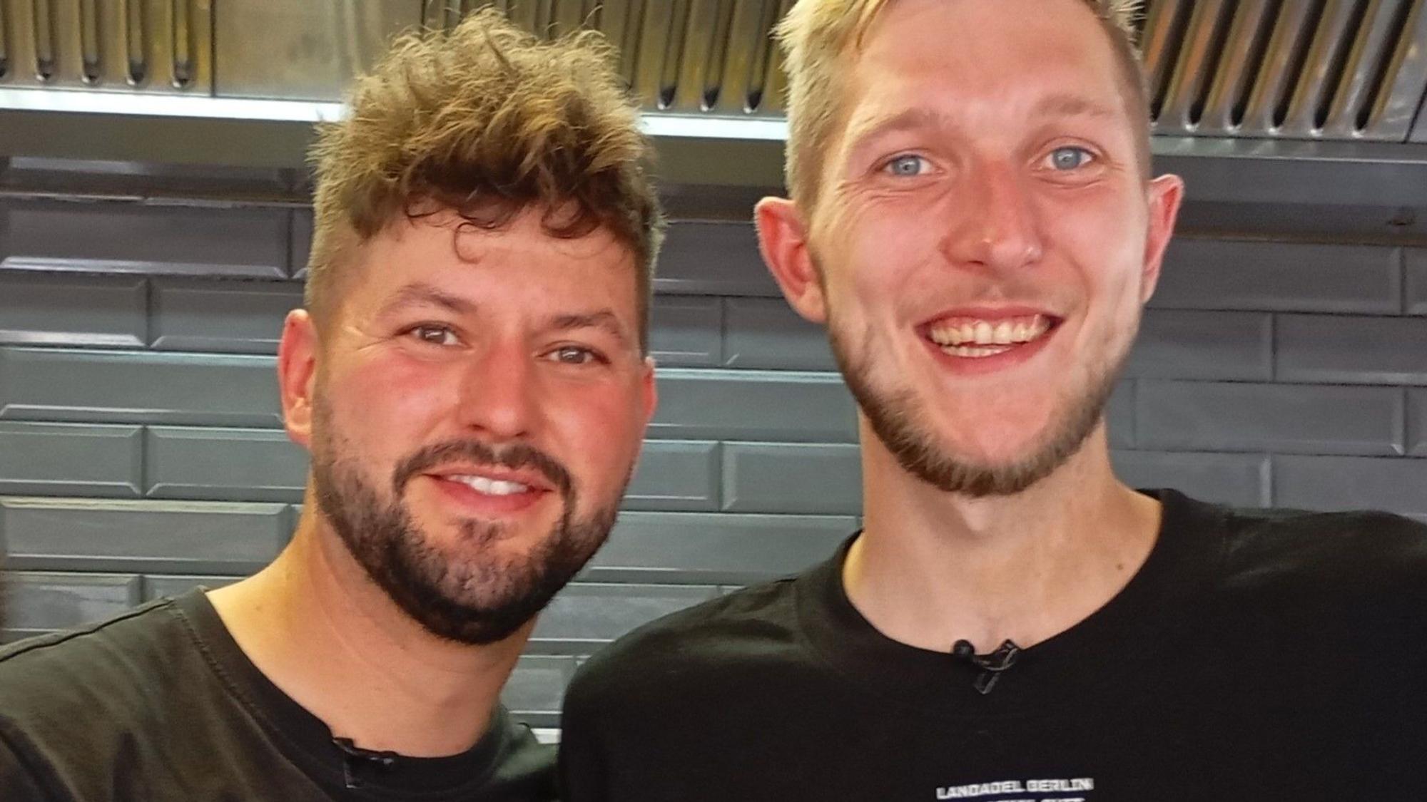 Auf dem Bild sind zwei junge Männer in schwarzen T-Shirts zu sehen.