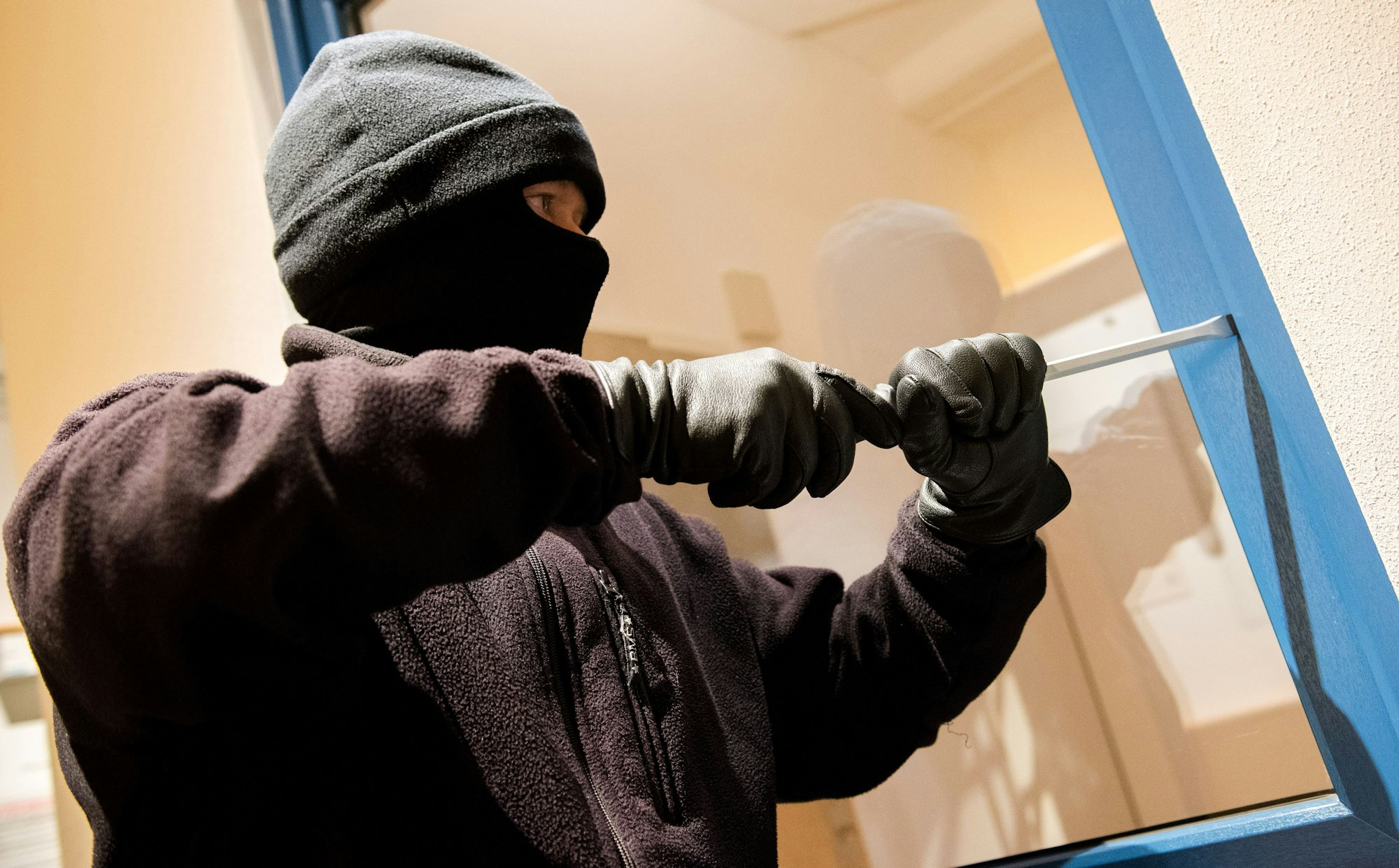 Ein Einbrecher hebelt ein Fenster mit einem Schraubenzieher auf.