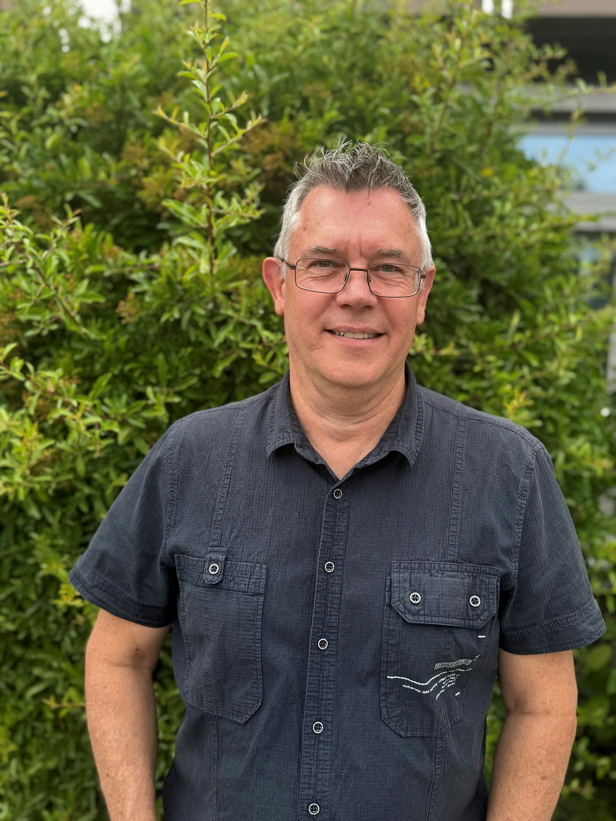 Ein Mann im dunkelgrauen Hemd guckt in die Kamera.