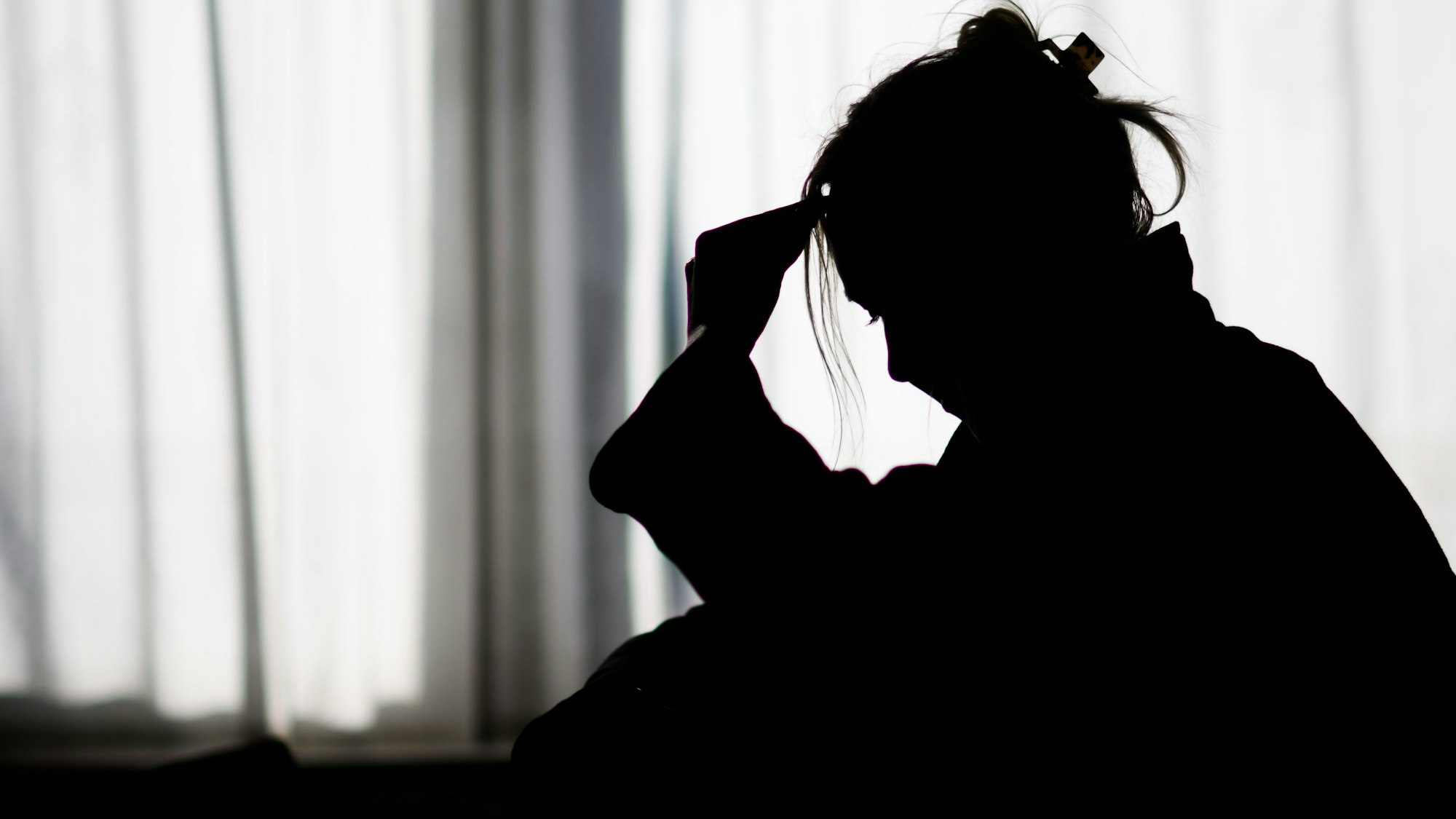 Das Foto zeigt die Silhouette einer Frau vor einer hellen Fensterfront.