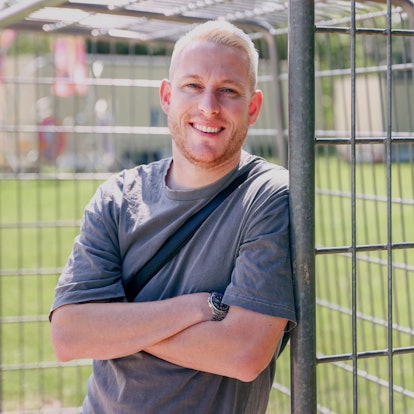 Ein Mann mit blonder Kurzhaarfrisur lehnt an einem Fußballtor in einer Grünanlage.