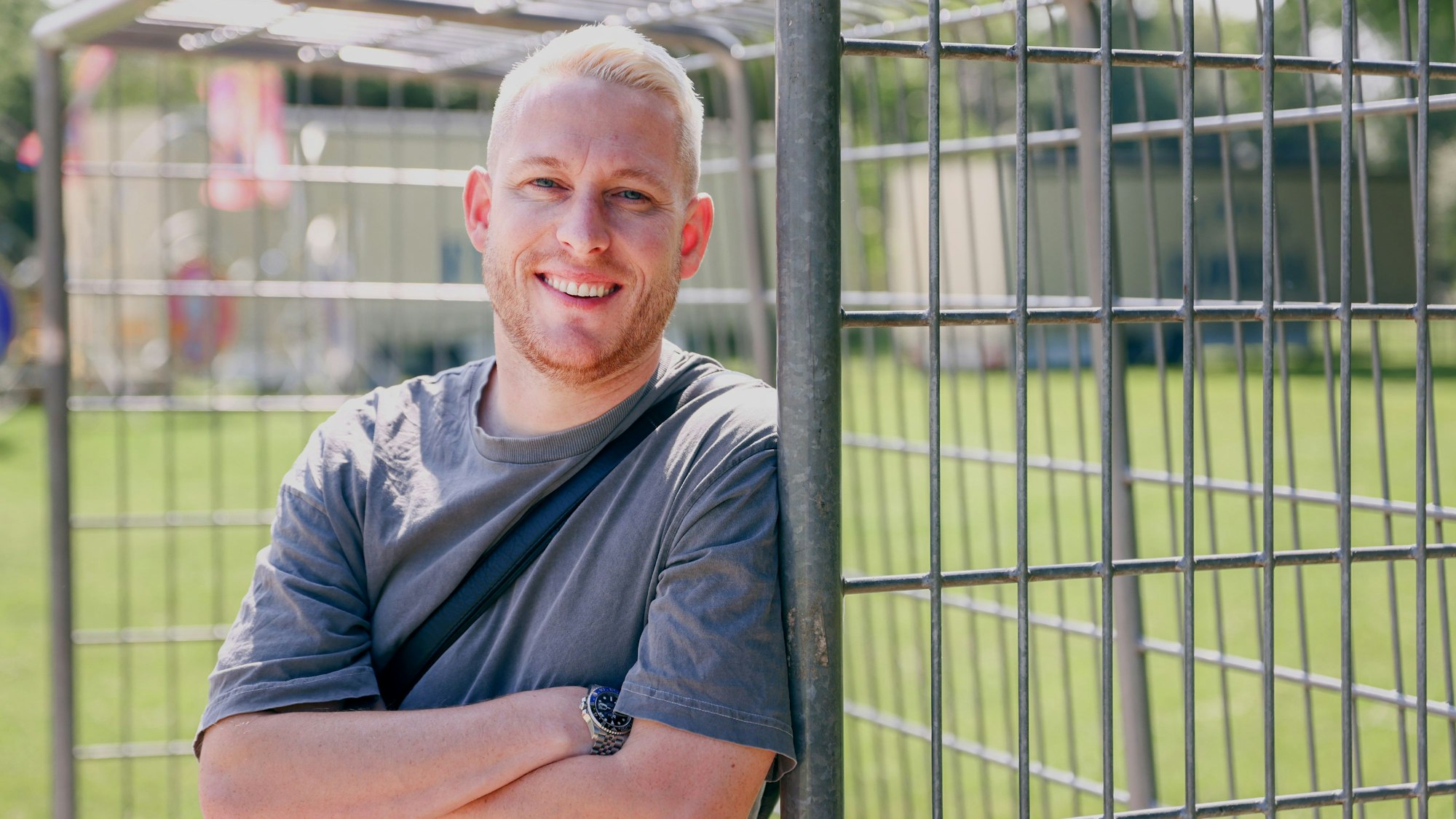 Ein Mann mit blonder Kurzhaarfrisur lehnt an einem Fußballtor in einer Grünanlage.
