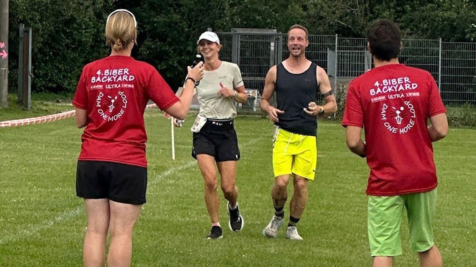 Christine Becker und Markus Habermann laufen nebeneinander ins Ziel, wo ein Mann und eine Frau in Biber-Backyard-T-Shirts warten.