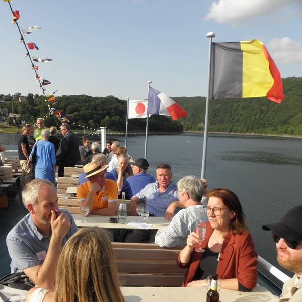 Die Teilnehmer sitzen an den Außentischen an Deck eines Rursee-Ausflugsschiffs.