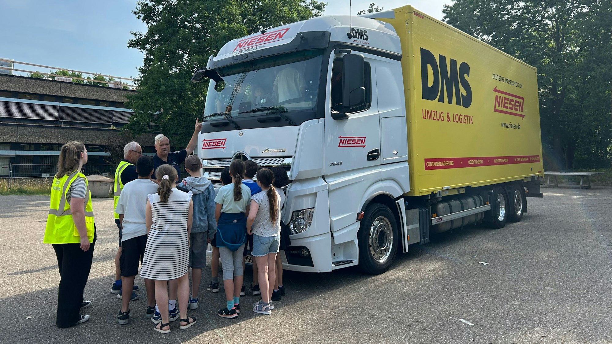 Polizeioberhauptkommissar Andreas Hetzert von der Verkehrsunfallprävention Köln (hinten im Bild) zeigt den Kindern einen der Außenspiegel des LKWs der Firma Niesen
