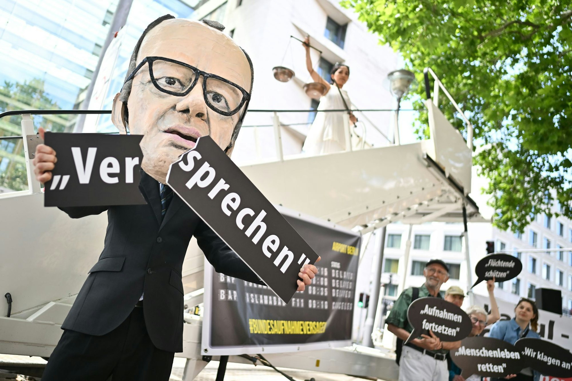 Ein Aktivist mit Merz-Maske zerbricht während einer symbolischen Protestaktion von Kabul Luftbrücke und Campact ein Schild mit der Aufschrift «Versprechen».