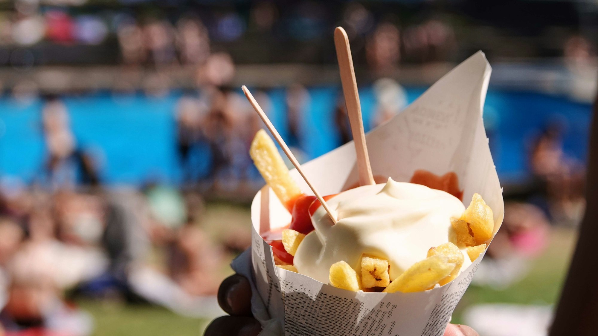 Ein Badegast hält eine Portion Pommes Frites mit Ketchup und Mayonnaise im Freibad.