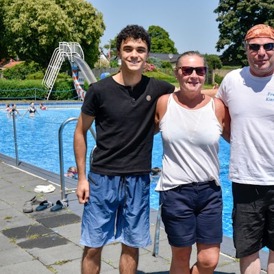 Vier Menschen stehen vor einem Schwimmbecken in Freien.