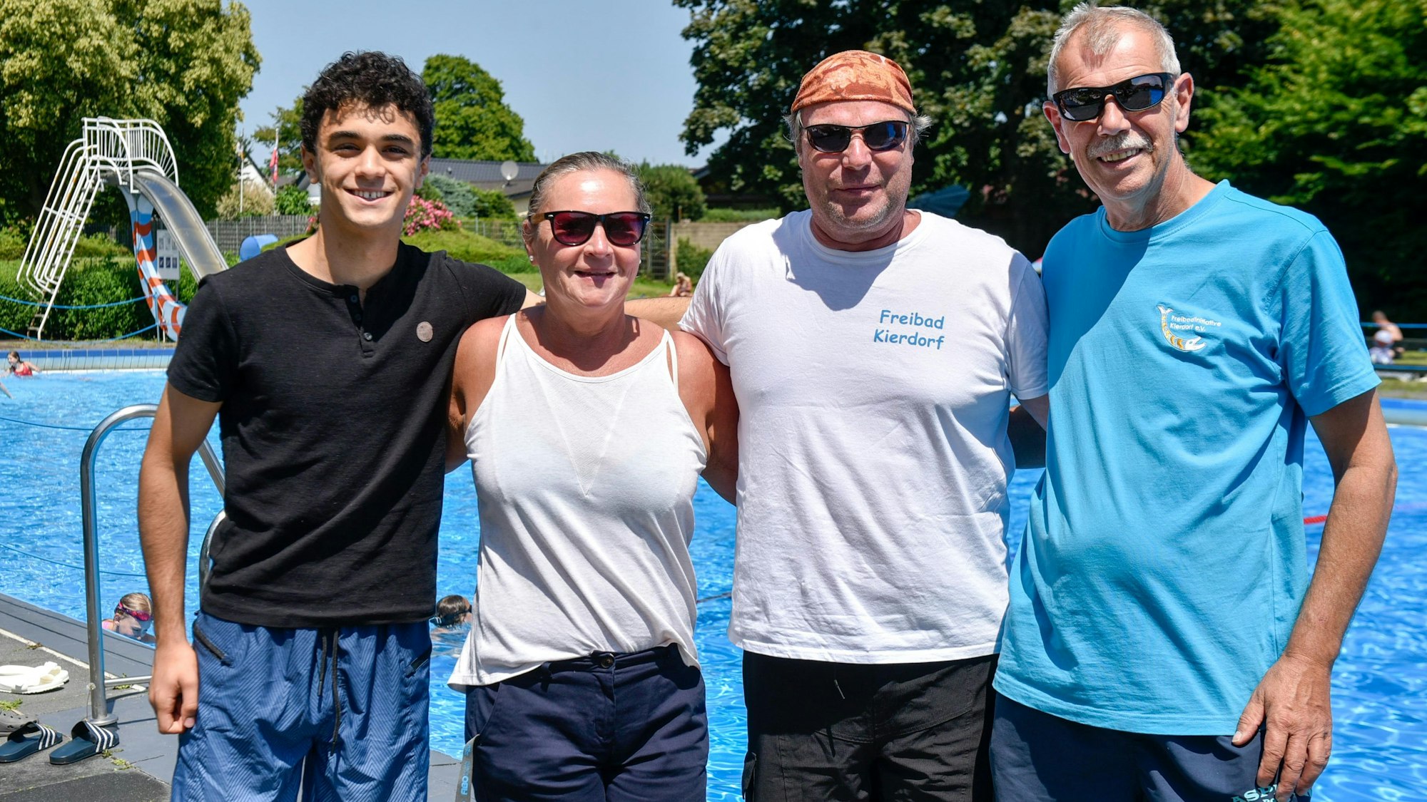 Vier Menschen stehen vor einem Schwimmbecken in Freien.
