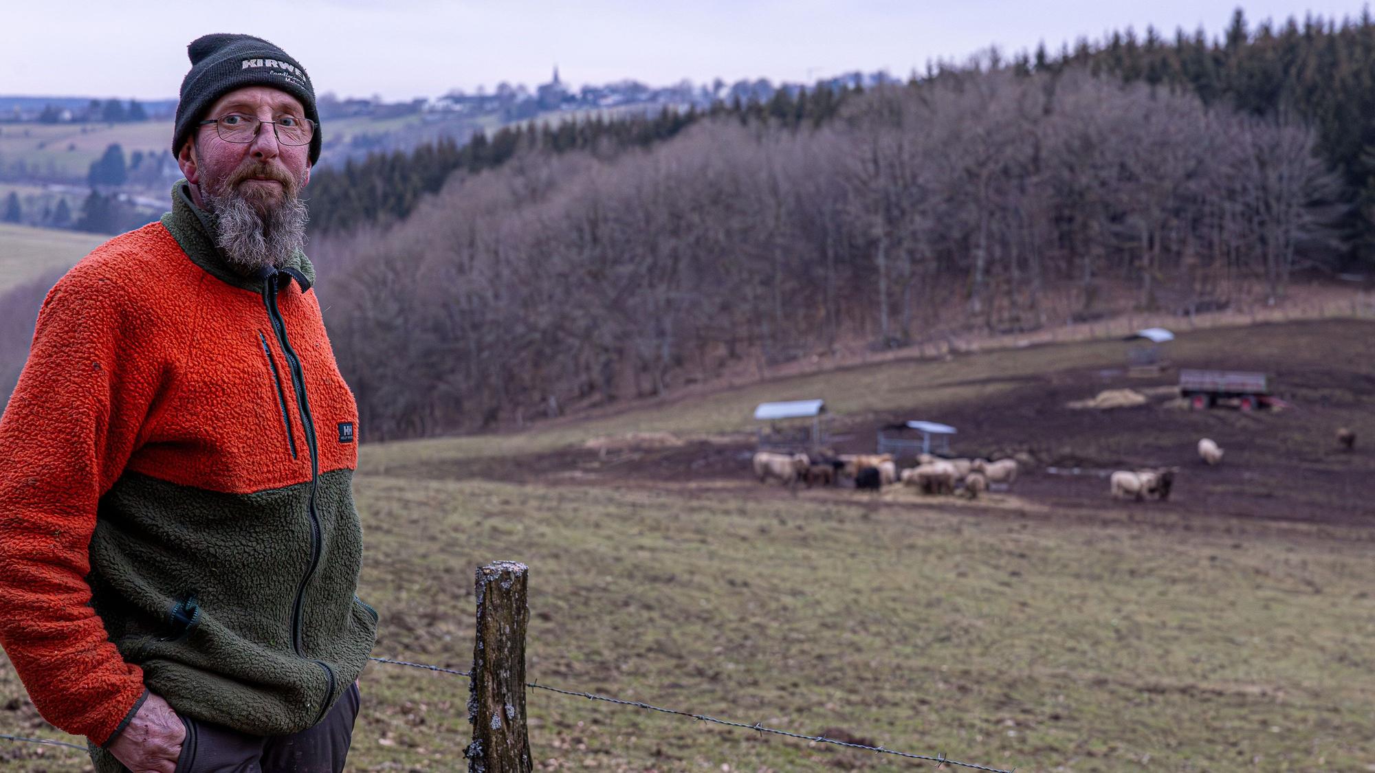 Der Landwirt steht an einer Weide, auf der er Schottische Hochlandrinder sim Winter hält. Auf den Höhen ist der Hellenthaler außenort Rescheid zu sehen.