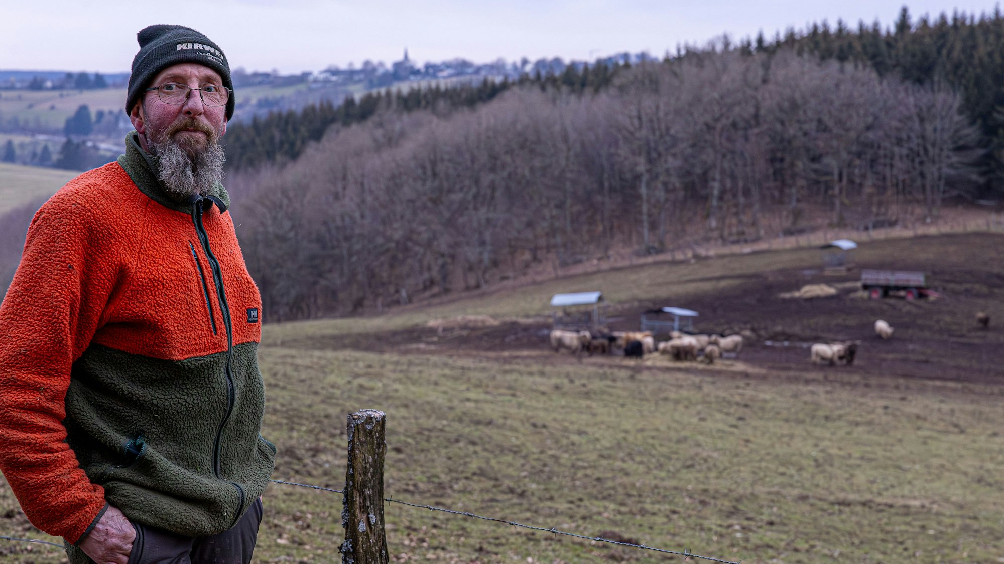Der Landwirt steht an einer Weide, auf der er Schottische Hochlandrinder sim Winter hält. Auf den Höhen ist der Hellenthaler außenort Rescheid zu sehen.