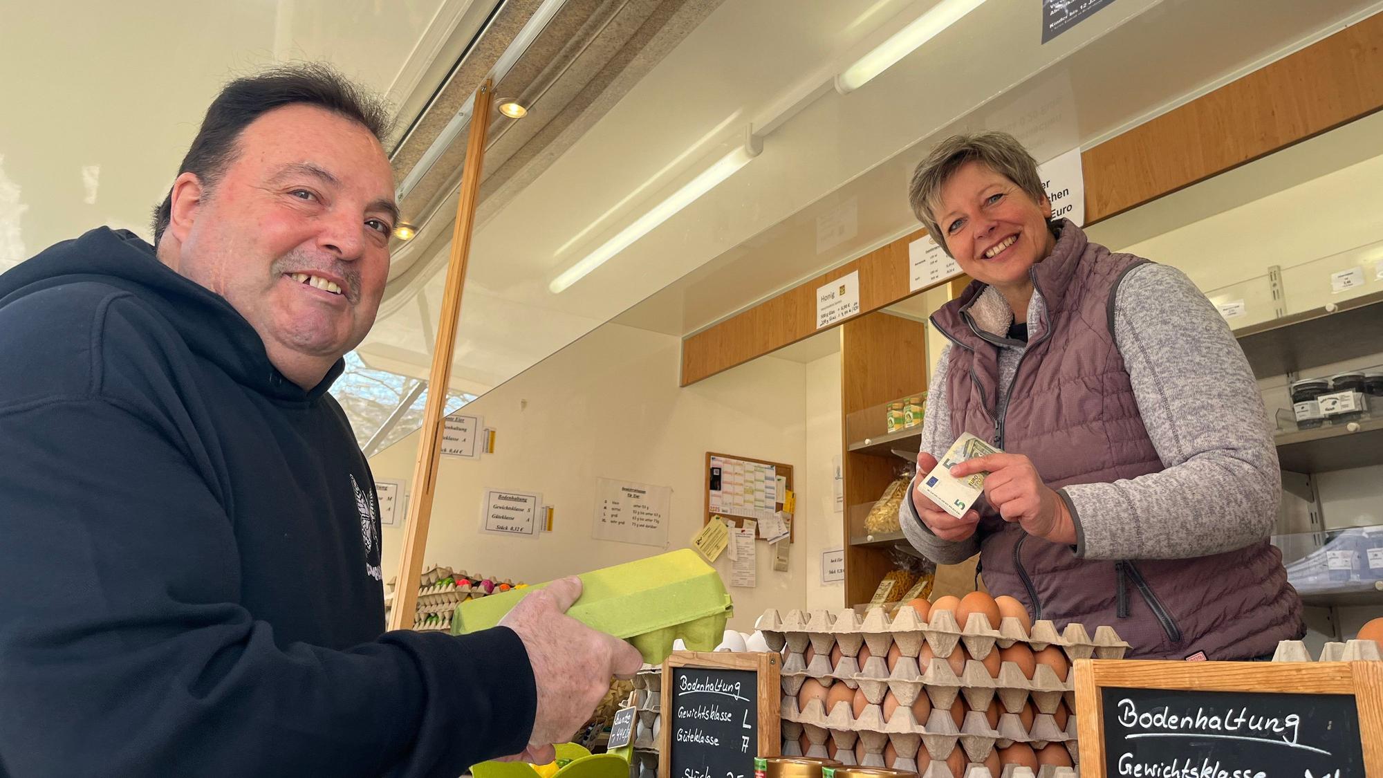 Ein Mann kauft bei einer Frau an einem Marktstand Eier.