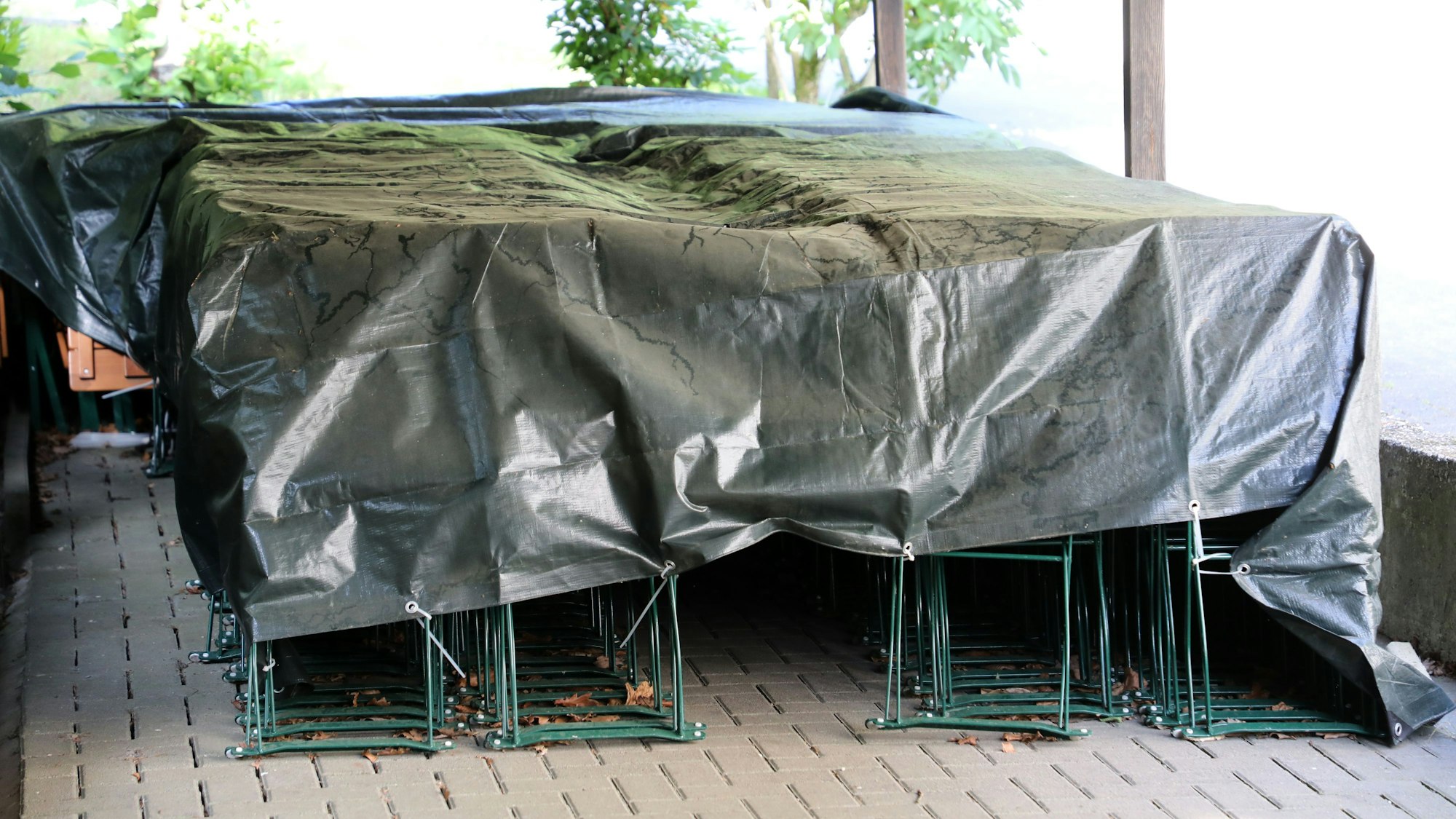 Unter Planen stehen Stühle und Tische der Waldwirtschaft Forsbacher Mühle.