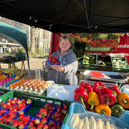 Eine Frau steht hinter ein Marktstand für Obst und Gemüse.