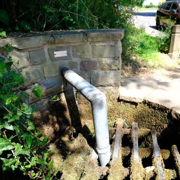An einem Brunnen ist das Auslassrohr des Wassers bis unter ein Gitter verlängert worden, um die Wasserentnahme zu verhindern.