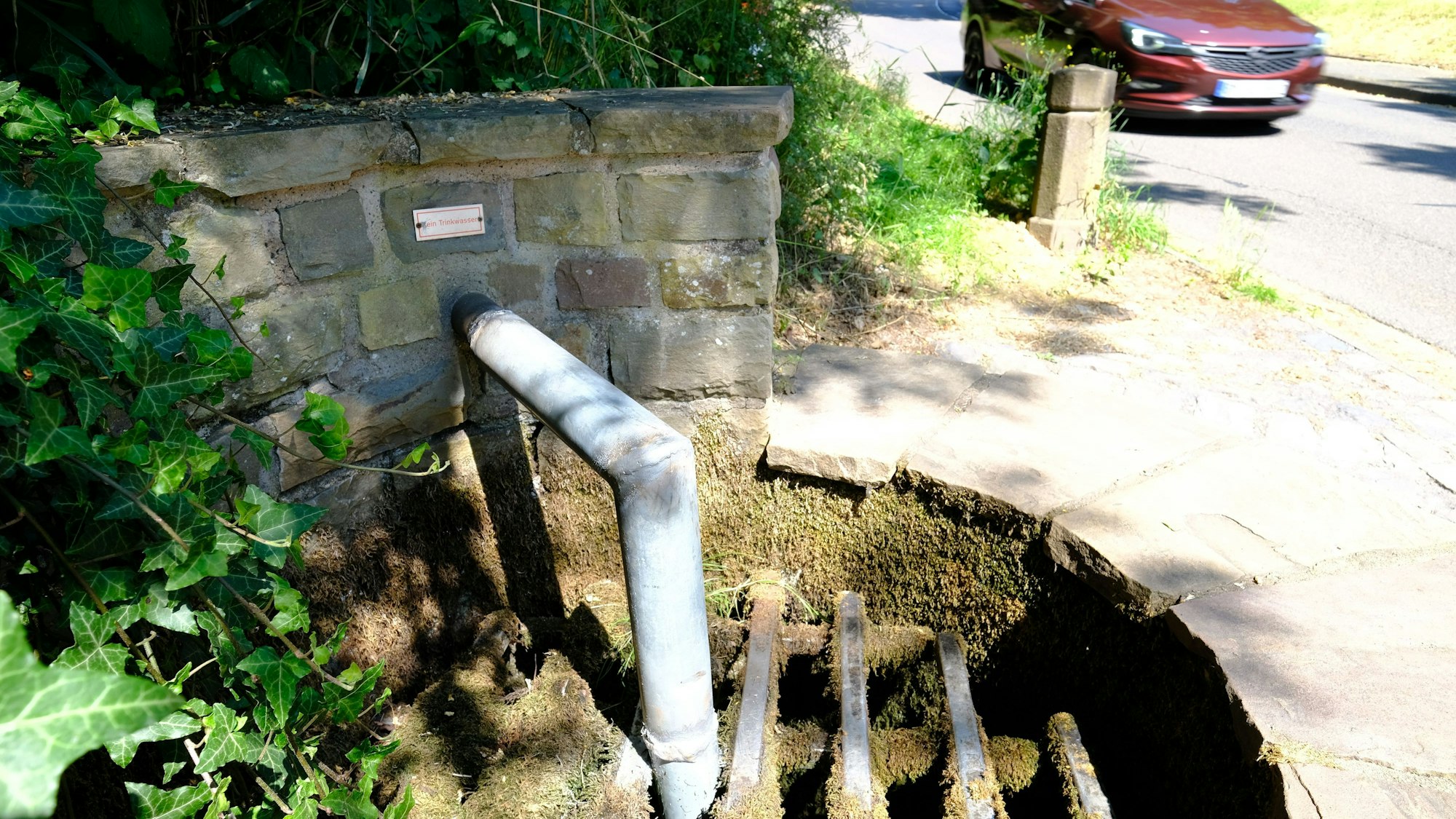 An einem Brunnen ist das Auslassrohr des Wassers bis unter ein Gitter verlängert worden, um die Wasserentnahme zu verhindern.