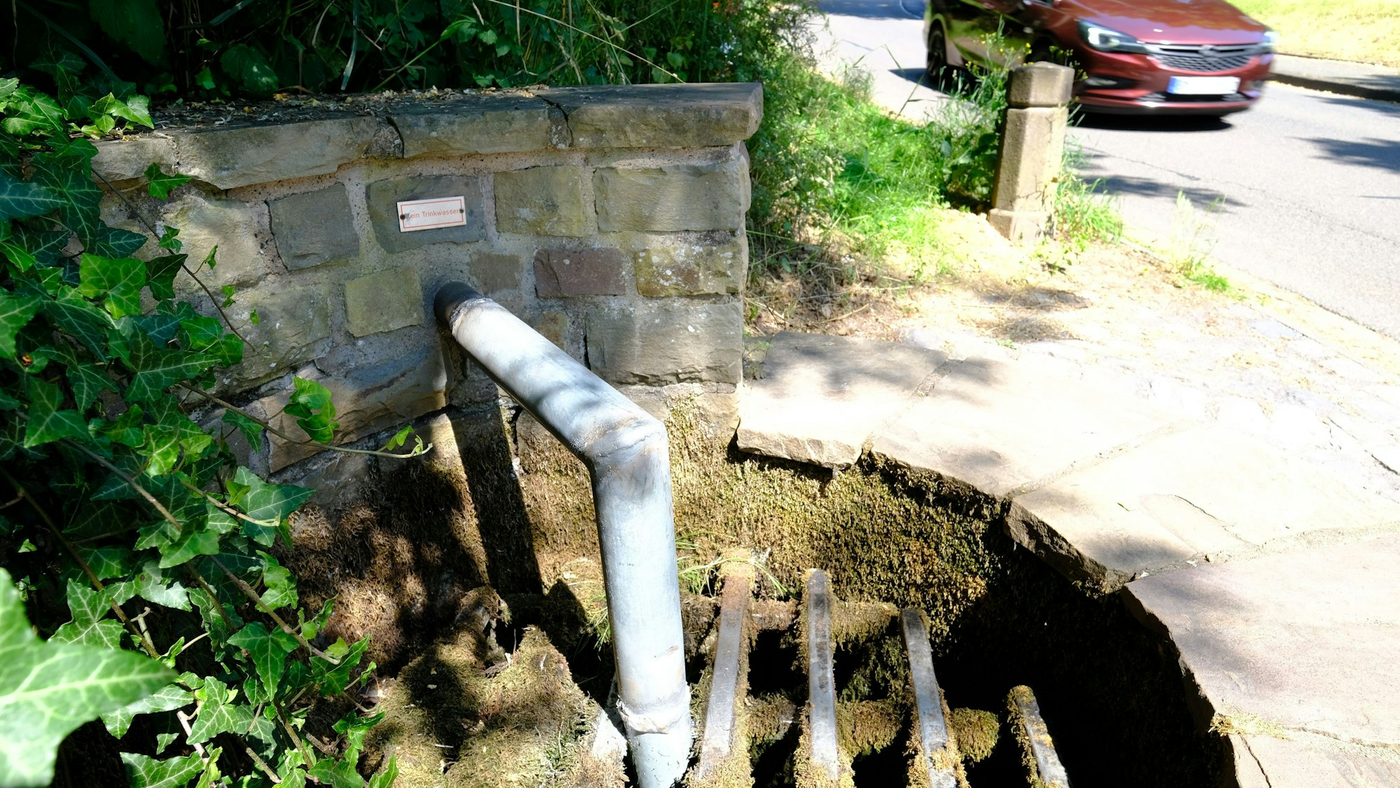 An einem Brunnen ist das Auslassrohr des Wassers bis unter ein Gitter verlängert worden, um die Wasserentnahme zu verhindern.