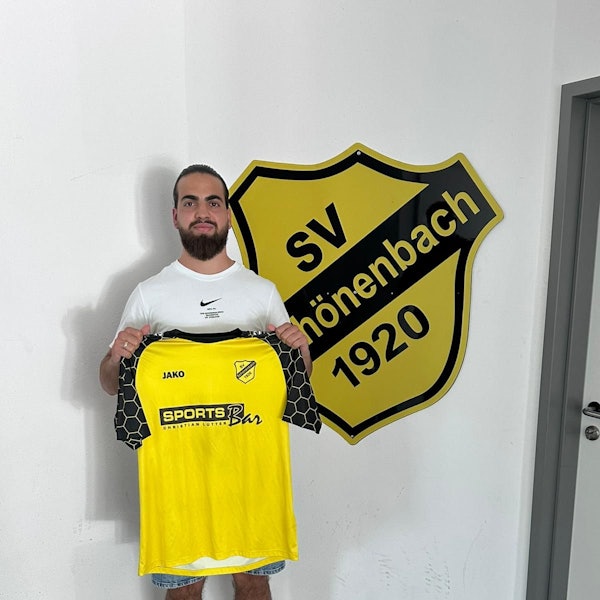Louis Vedder steht mit dem Schönenbacher Trikot in der Hand vor dem Vereinsabzeichen.