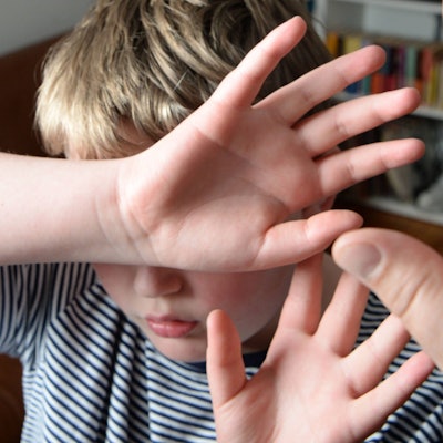 Ein Junge versucht sich vor den Schlägen seines Vaters zu schützen, indem er seine Hände vor sein Gesicht hält.