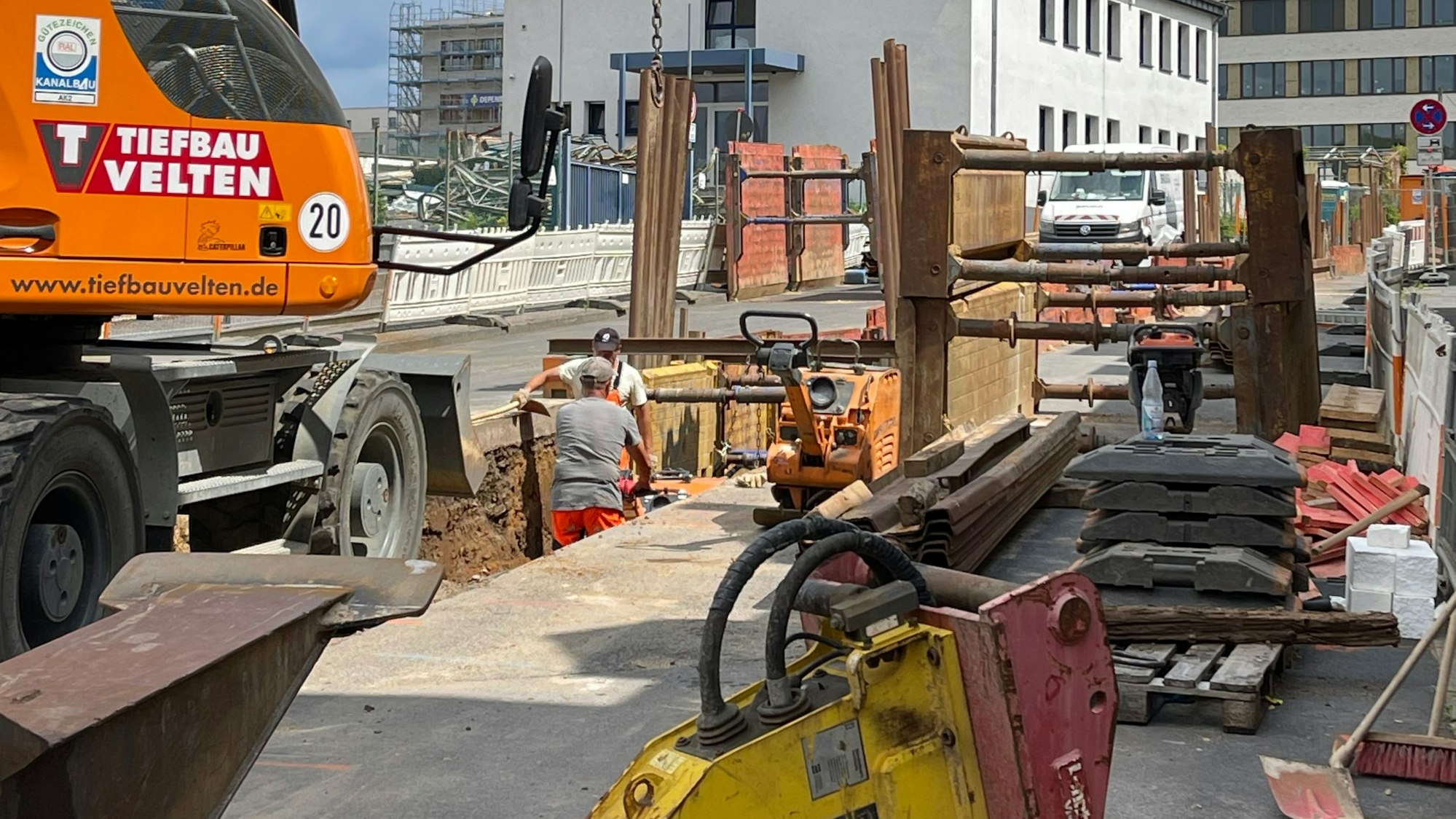 Das Bild zeigt eine Baustelle mit aufgebrochener Straße, Bagger und Arbeitern.
