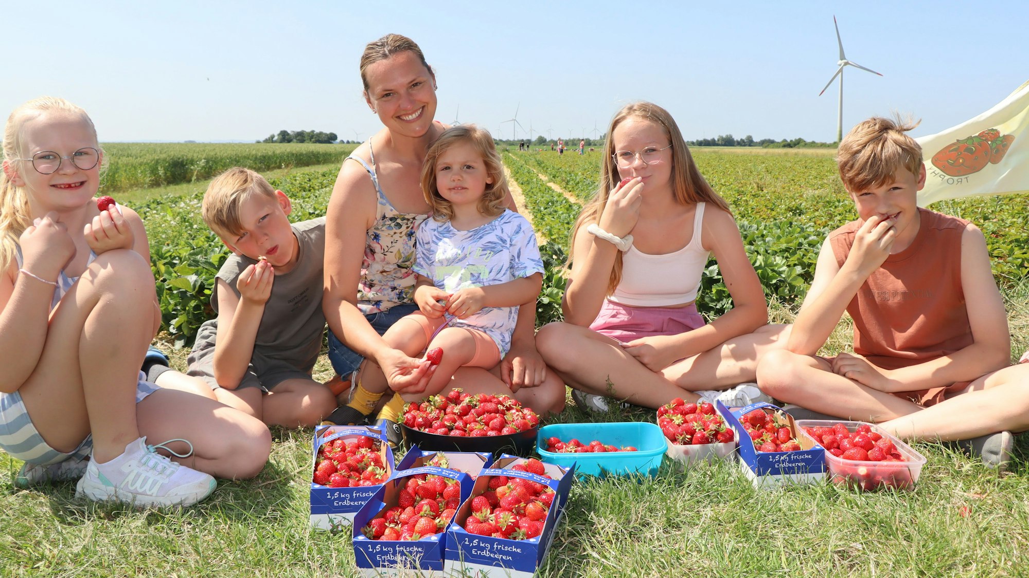 Auf dem Bild ist ein Frau mit Kindern zu sehen, sie zeigen ihre Erdbeerernte.